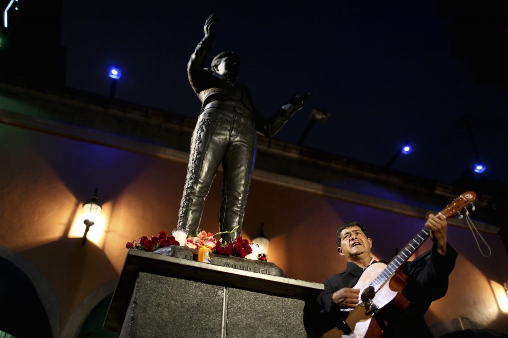 Un músico interpreta una canción delante de la imagen del cantante y compositor mexicano Juan Gabriel en la Plaza Garibaldi, el 28 de agosto de 2016, en la Ciudad de México. Crédito: YURI CORTEZ / AFP / Getty Images.