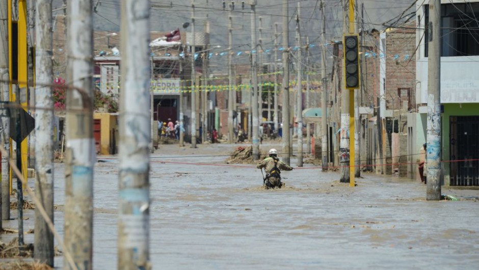 A rescue workers waits to help local residents of the town of Huarmey, 300 kilometres north of Lima, wade through muddy water on the street on March 19, 2017 after a flash flood hit the evening before. The El Nino climate phenomenon is causing muddy rivers to overflow along the entire Peruvian coast, isolating communities and neighbourhoods. Thousands have been affected since January, and 72 people have died. Most cities face water shortages as water lines have been compromised by mud and debris. / AFP PHOTO / CRIS BOURONCLE (Photo credit should read CRIS BOURONCLE/AFP/Getty Images)