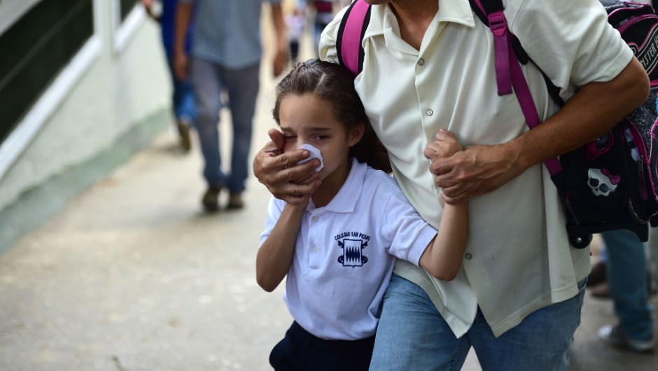 TOPSHOT - A schoolgirl covers her nose and mouth to avoid breathing tear gas shot by police at opponents of Venezuelan President Nicolas Maduro marching in Caracas on April 26, 2017. Protesters in Venezuela plan a high-risk march against President Maduro Wednesday, sparking fears of fresh violence after demonstrations that have left 26 dead in the crisis-wracked country. / AFP PHOTO / RONALDO SCHEMIDT (Photo credit should read RONALDO SCHEMIDT/AFP/Getty Images)