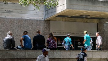 People remain outside the headquarters of the Central Bank of Venezuela, in Caracas, on January 28, 2019. - Venezuela devalued its currency by almost 35 percent on Monday to bring it into line with the exchange rate of the dollar on the black market. The exchange rate is now fixed at 3,200 bolivars to the dollar, almost matching the 3,118.62 offered on the dolartoday.com site that acts as the reference for the black market. (Photo by LUIS ROBAYO / AFP) (Photo credit should read LUIS ROBAYO/AFP/Getty Images)
