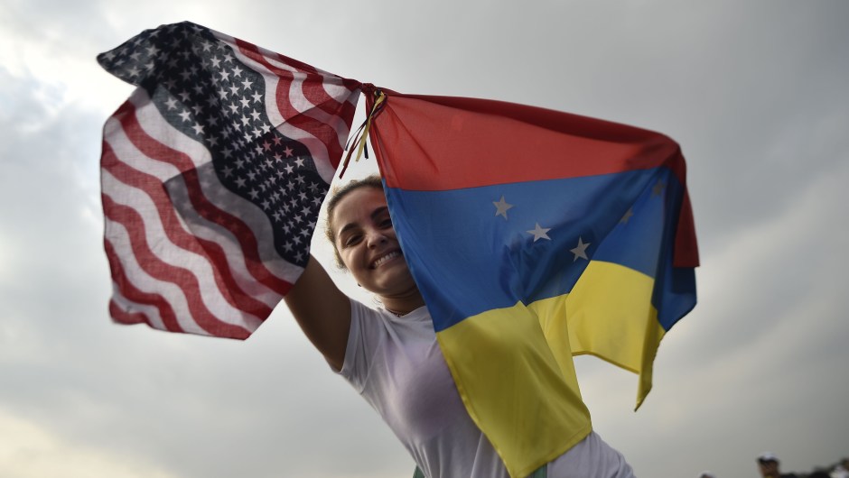 A woman holds the Venezuelan and US flags as she waits for the start of "Venezuela Aid Live" concert, organized by British billionaire Richard Branson to raise money for the Venezuelan relief effort at Tienditas International Bridge in Cucuta, Colombia, on February 22, 2019 - The concert was organized by British billionaire Richard Branson to raise money for the Venezuelan relief effort. Venezuela's political tug-of-war morphs into a battle of the bands on Friday, with dueling government and opposition pop concerts ahead of a weekend showdown over the entry of badly needed food and medical aid. (Photo by Luis ROBAYO / AFP) (Photo credit should read LUIS ROBAYO/AFP/Getty Images)