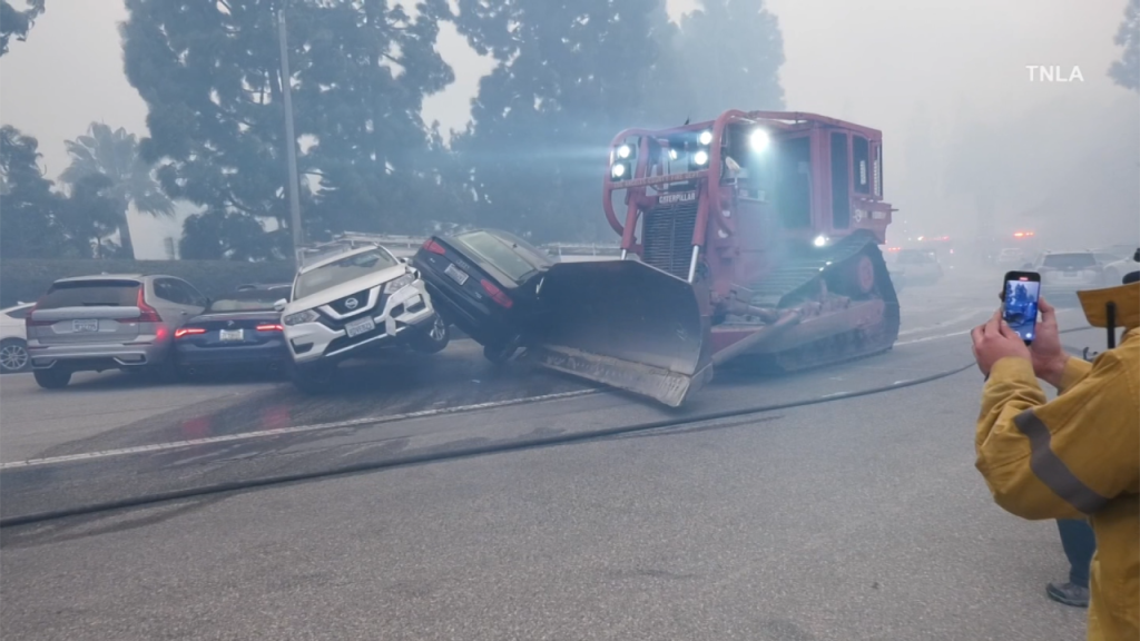 Una excavadora se abre paso entre automóviles abandonados en medio del caos provocado por el incendio forestal de Los Ángeles